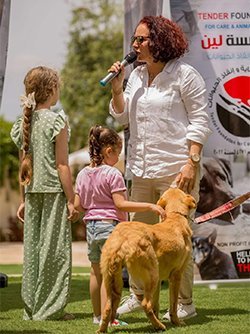 A woman speaking into a microphone with two children and a dog during an outdoor animal care event.